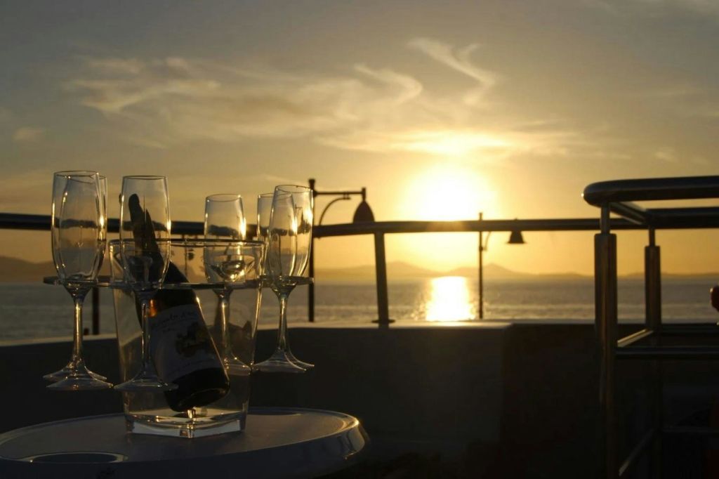 샴페인 잔과 앞쪽 테이블에 놓인 병이 있는 물 위에서 석양을 감상할 수 있습니다.
