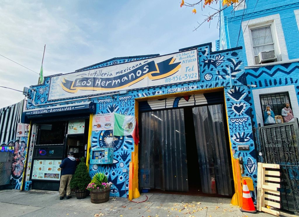 Tortilleria Mexicana Los Hermanos의 화려한 상점가에는 활기찬 벽화와 바깥에 있는 멕시코 국기가 있습니다.