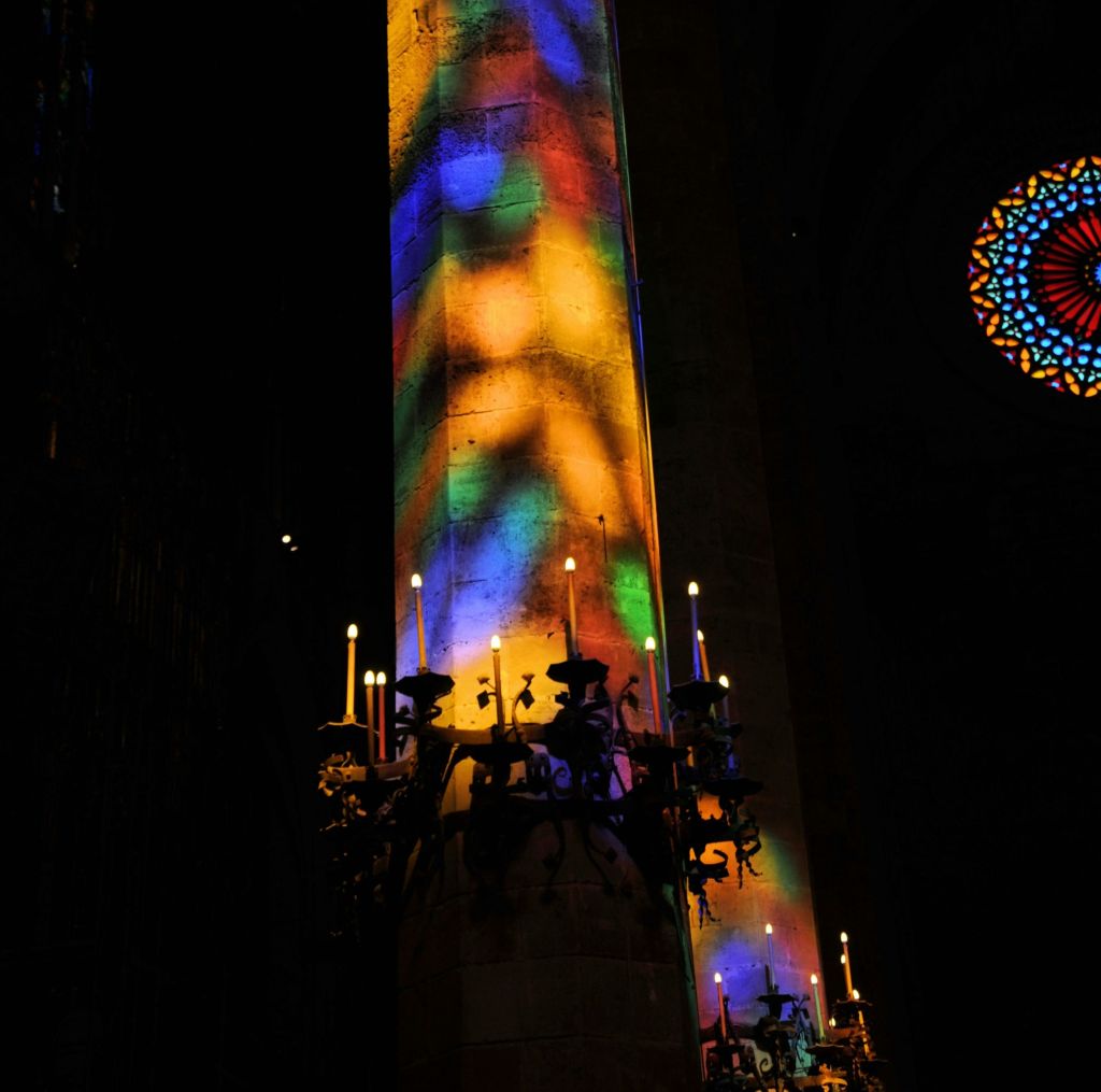 화려한 촛불 홀더에 촛불이 달린 어두운 교회의 커다란 기둥에 화려한 조명 패턴이 비추고 있습니다.