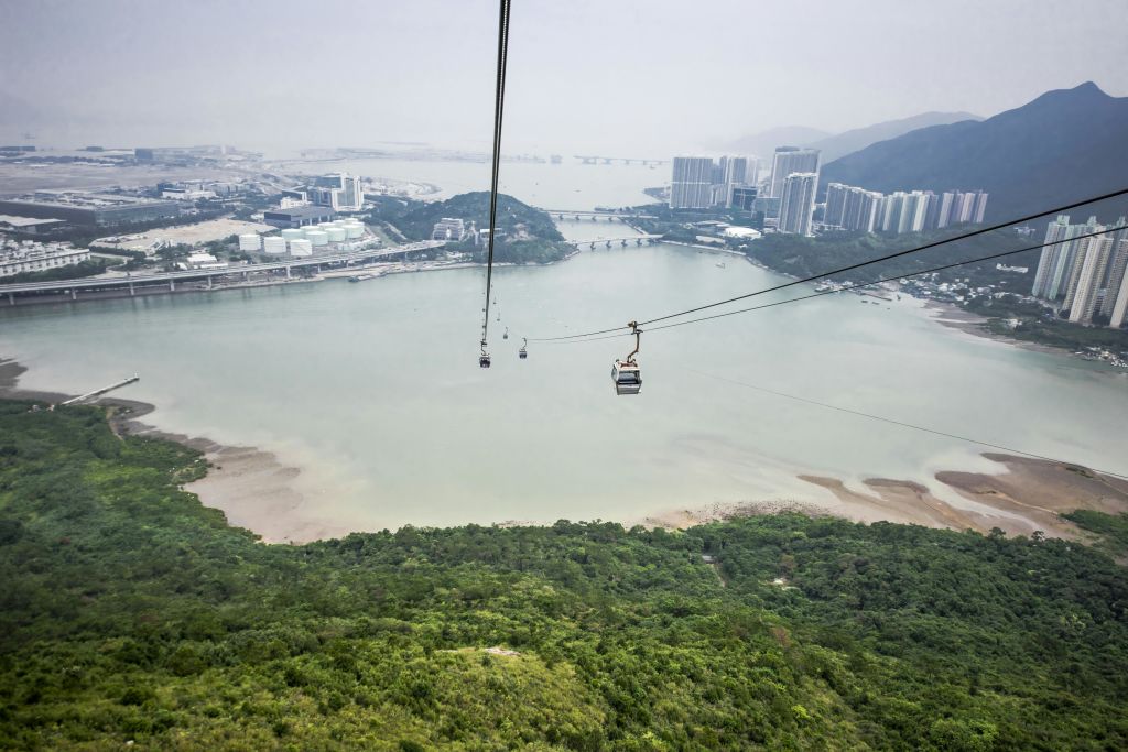 푸른 언덕과 흐릿한 하늘을 배경으로 도시 풍경을 배경으로 물 위에 매달린 케이블카.