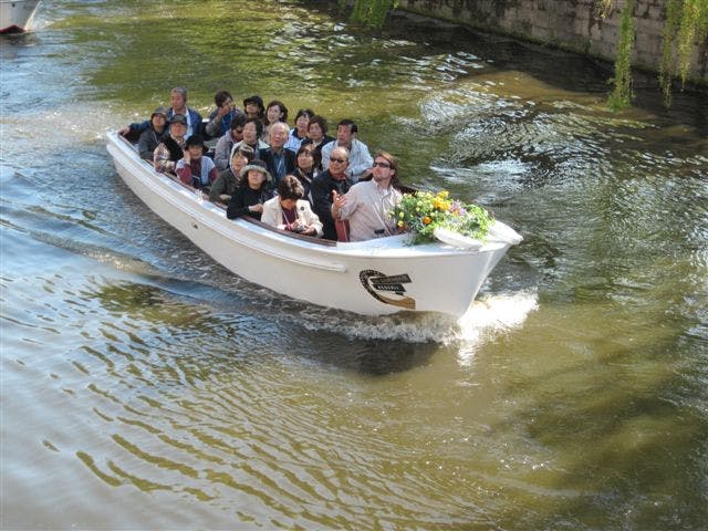 운하를 따라 순항하는 하얀 보트에 앉아 있는 한 무리의 사람들. 보트 정면에 꽃꽂이가 있습니다.
