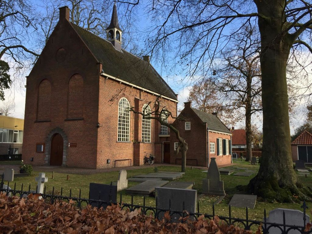 스테인드글라스 창문, 인접한 묘지, 잎이 없는 나무, 푸른 하늘이 있는 오래된 벽돌 교회. 일부 비석과 자전거 선물.