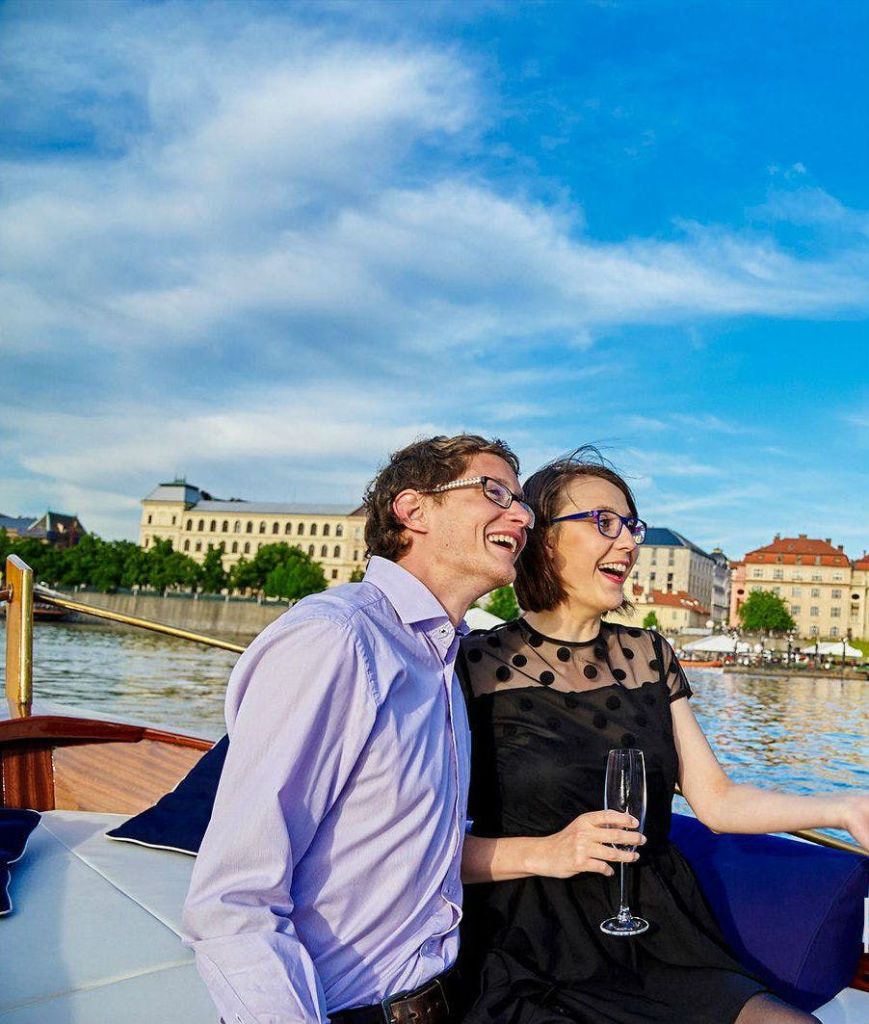 도시 풍경과 강을 배경으로 보트에 앉아 샴페인 한 잔을 들고 웃고 있는 커플.