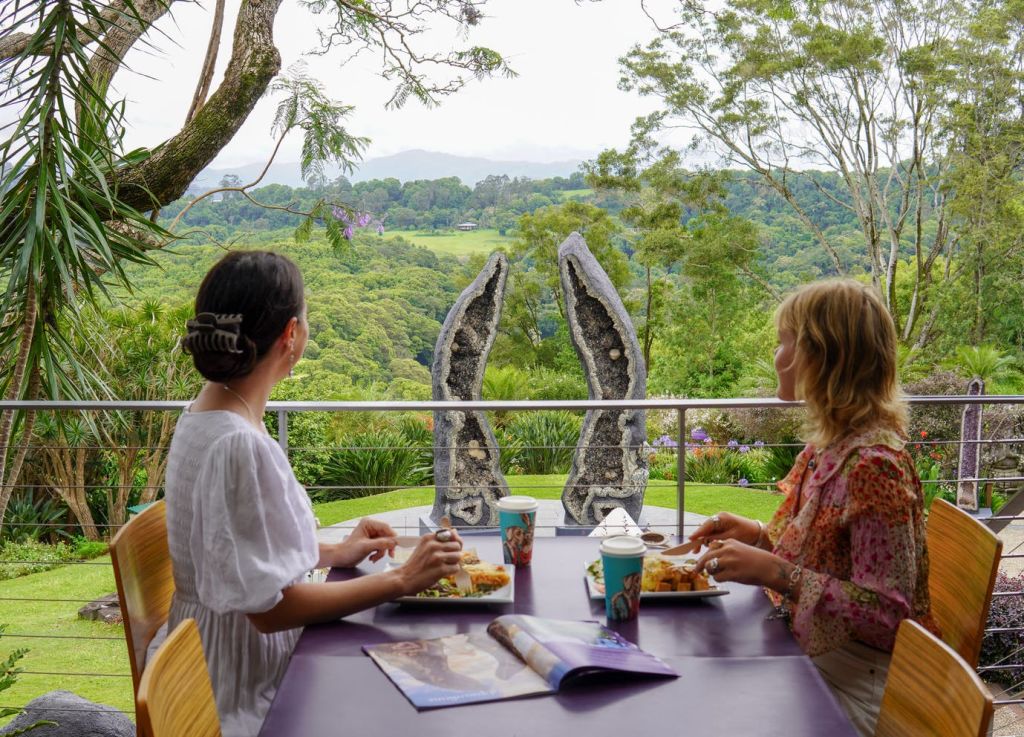 경치 좋은 녹색 풍경과 커다란 정동석 조각상이 내려다보이는 테이블에서 야외 식사를 즐기는 두 사람.