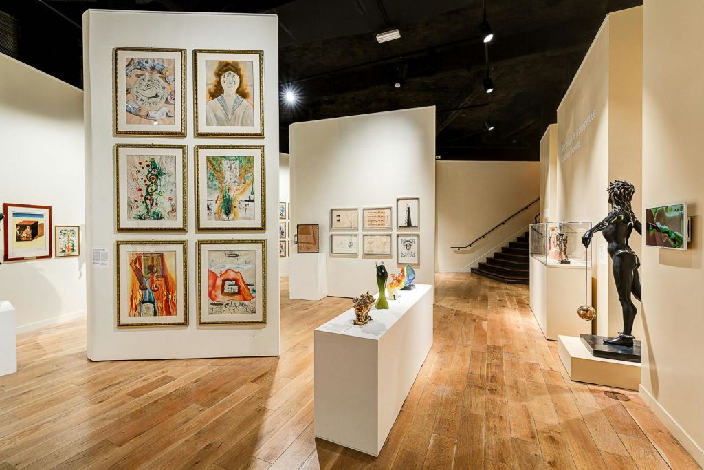 벽에 액자 그림, 받침대 조각, 나무 바닥, 계단을 배경으로 한 미술관.