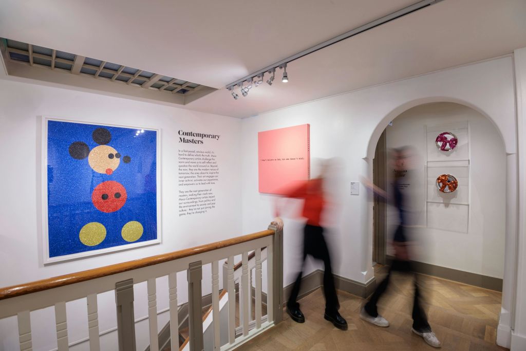 벽에 화려한 예술 작품이 걸려 있고, 계단과 흐릿한 형상이 걸어다니는 박물관 갤러리가 있습니다.