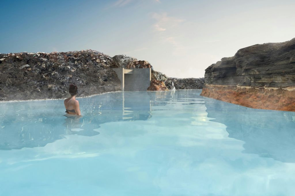 맑은 하늘 아래 바위 지형으로 둘러싸인 지열 수영장에 수영복을 입은 사람이 서 있습니다.