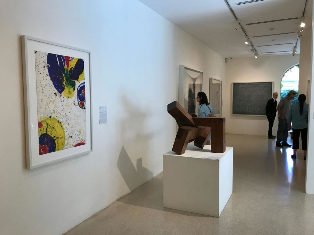 벽에 추상적인 그림이 있고 받침대에 나무 조각이 있는 현대 미술관입니다. 두 사람이 작품을 관찰합니다.