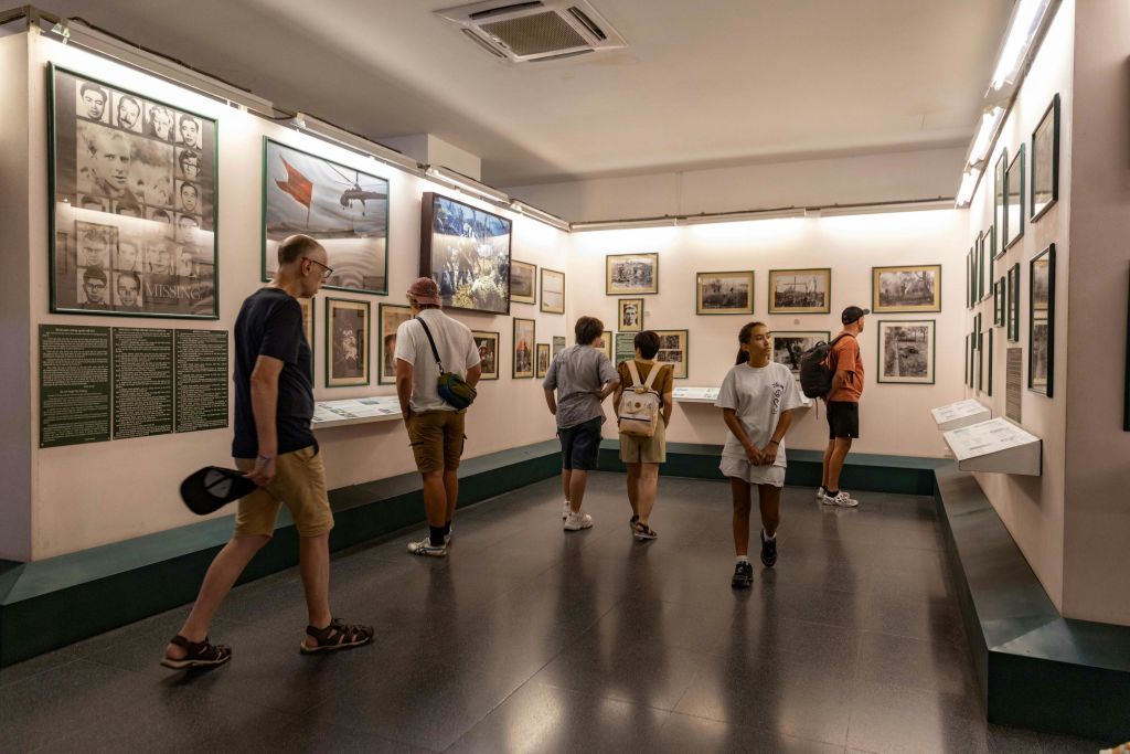 조명이 밝은 박물관 갤러리의 벽면에서 액자에 담긴 사진과 전시물을 감상하는 사람들.