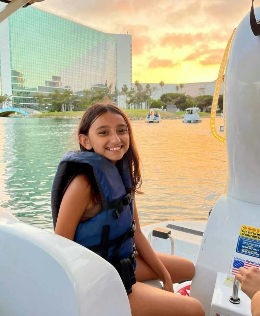 현대적인 건물과 석양을 배경으로 보트에서 구명조끼를 입은 미소 짓는 소녀.