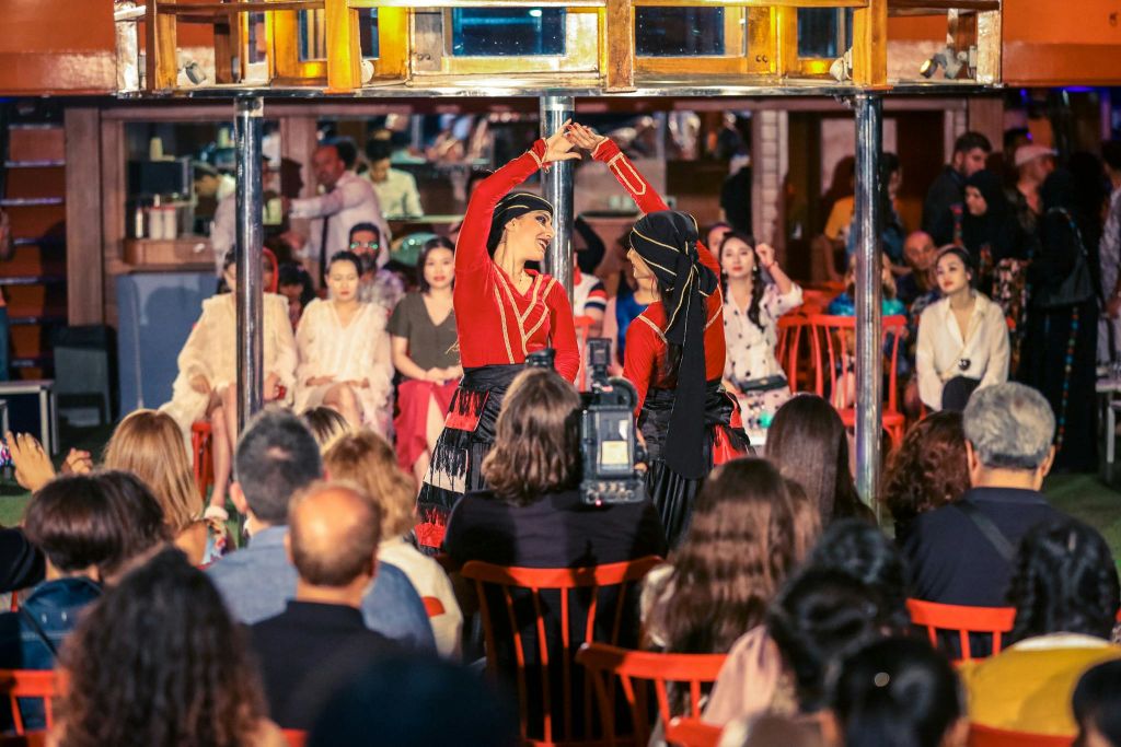 빨간색 의상을 입은 두 명의 댄서가 다채로운 실내 환경에서 관객들 앞에서 공연을 펼칩니다.