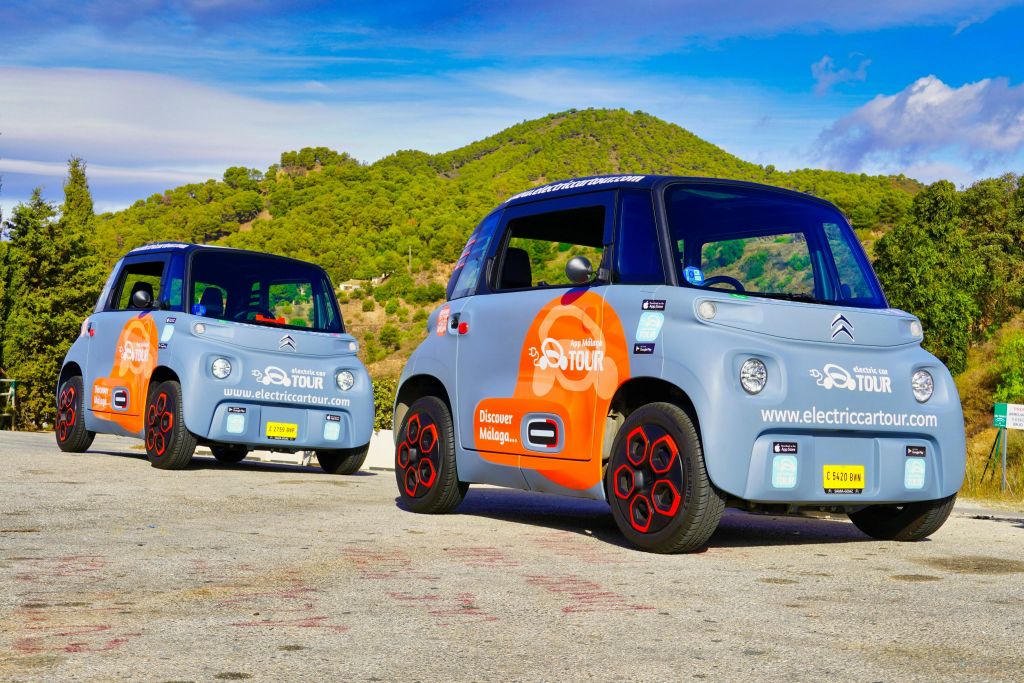 나무와 언덕을 배경으로 다채로운 색상의 전기 자동차 두 대가 도로에 주차되어 있습니다.