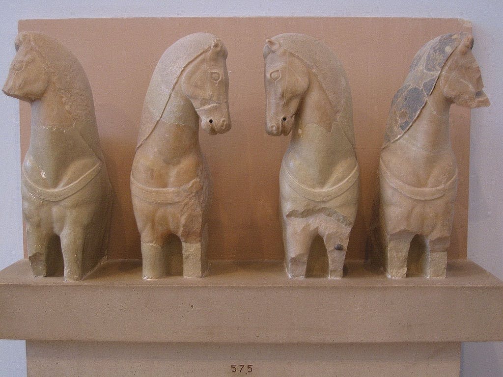 베이지색 선반에 전시된 4개의 고대 석조 말 조각상이 줄지어 있습니다.