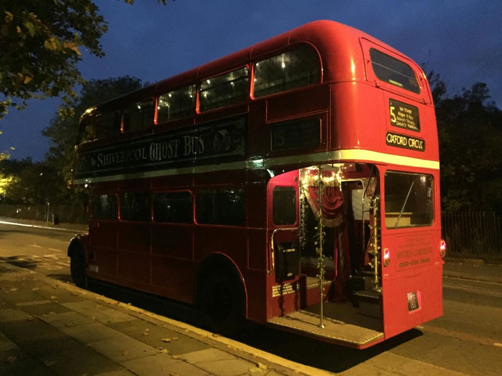 "고스트 버스" 표지판이 있는 빨간색 2층 버스는 해질 무렵에 문을 열고 내부 조명이 켜져 있습니다.