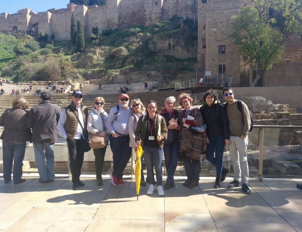 화창한 날, 고대 돌담과 유적 앞에 아홉 명의 사람들이 웃으며 함께 서 있습니다.