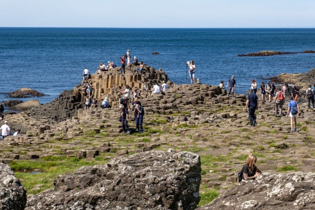 맑고 푸른 하늘 아래, 바닷가에 자리한 천연 암석 지층인 자이언트 코즈웨이를 둘러보는 관광객들.