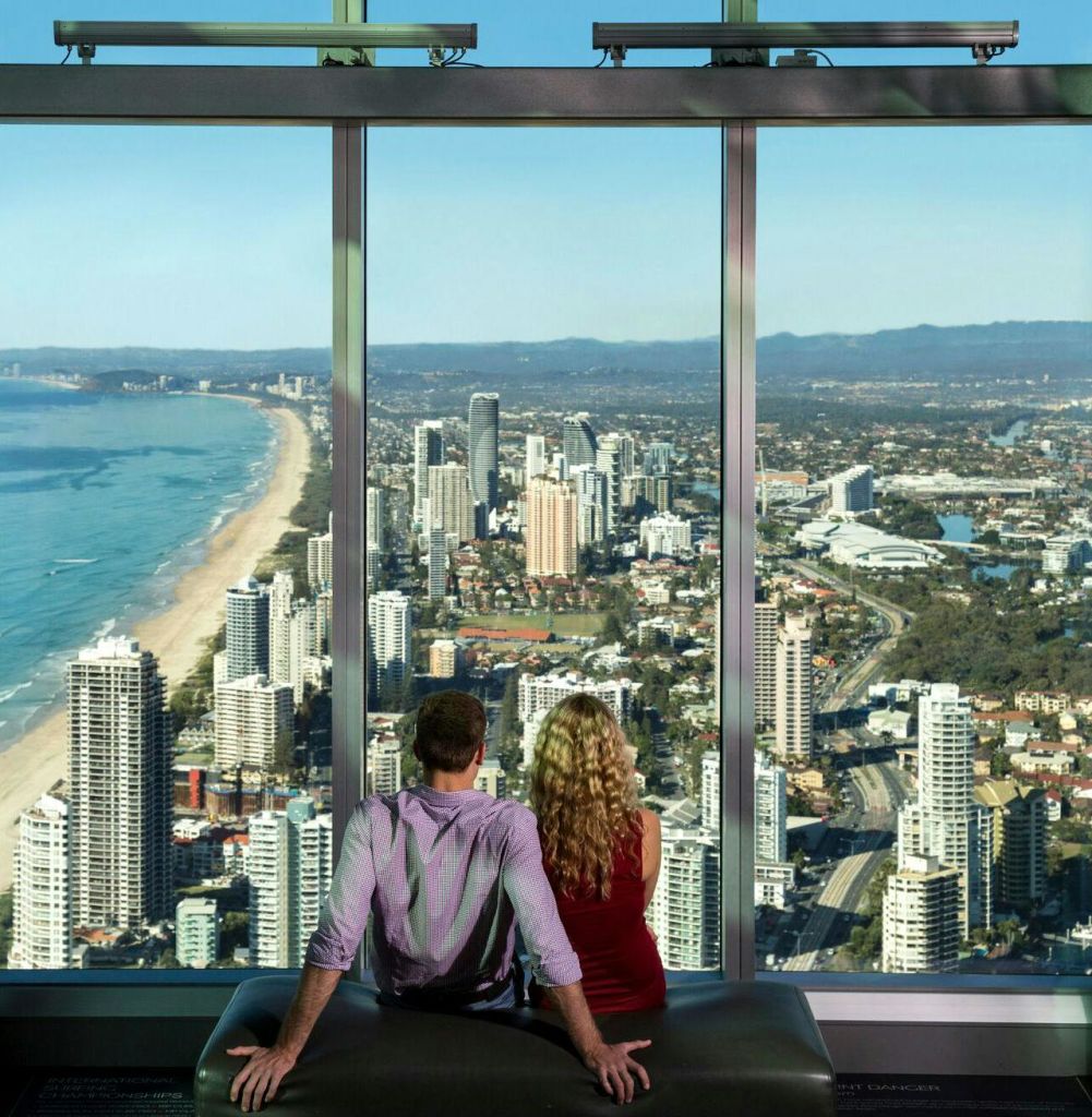 높은 건물과 해안선이 있는 도시 풍경을 바라보며 커다란 창문을 바라보는 남녀가 함께 앉아 있습니다.