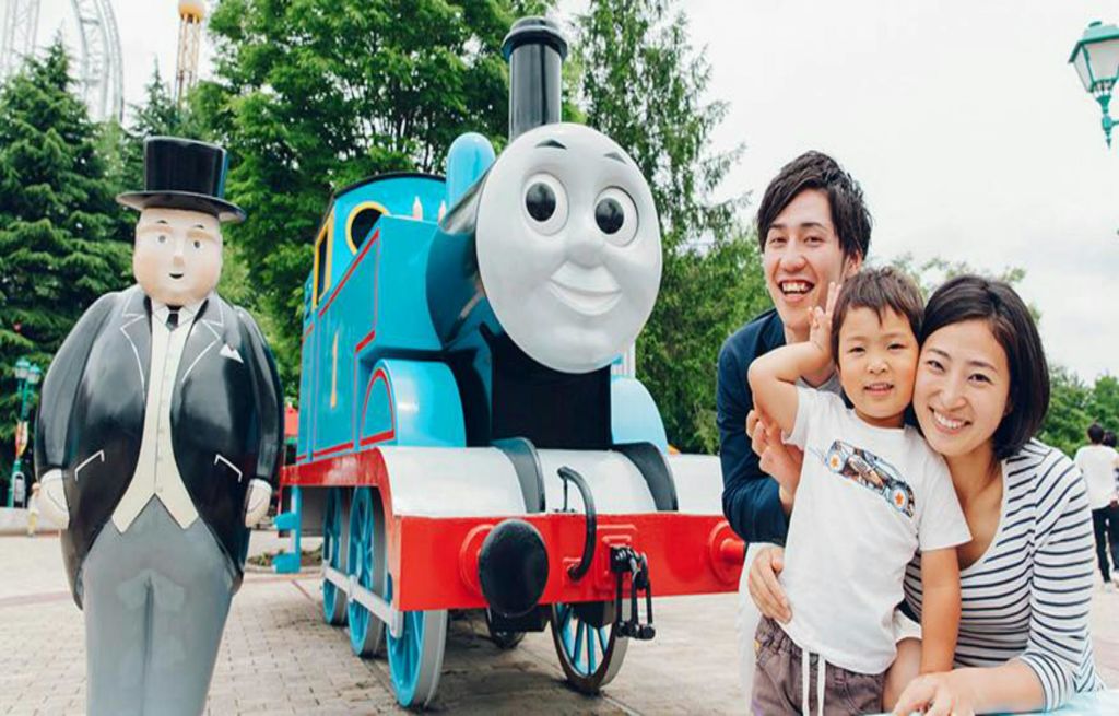 화창한 날 야외에서 대형 Thomas the Tank Engine 모델 앞에서 미소 짓는 가족이 포즈를 취하고 있습니다.