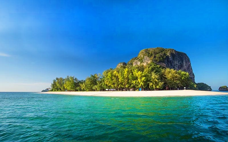 청록색 바다는 푸른 나무가 우거진 모래 해변과 밝고 푸른 하늘 아래 바위 언덕을 만나게 됩니다.