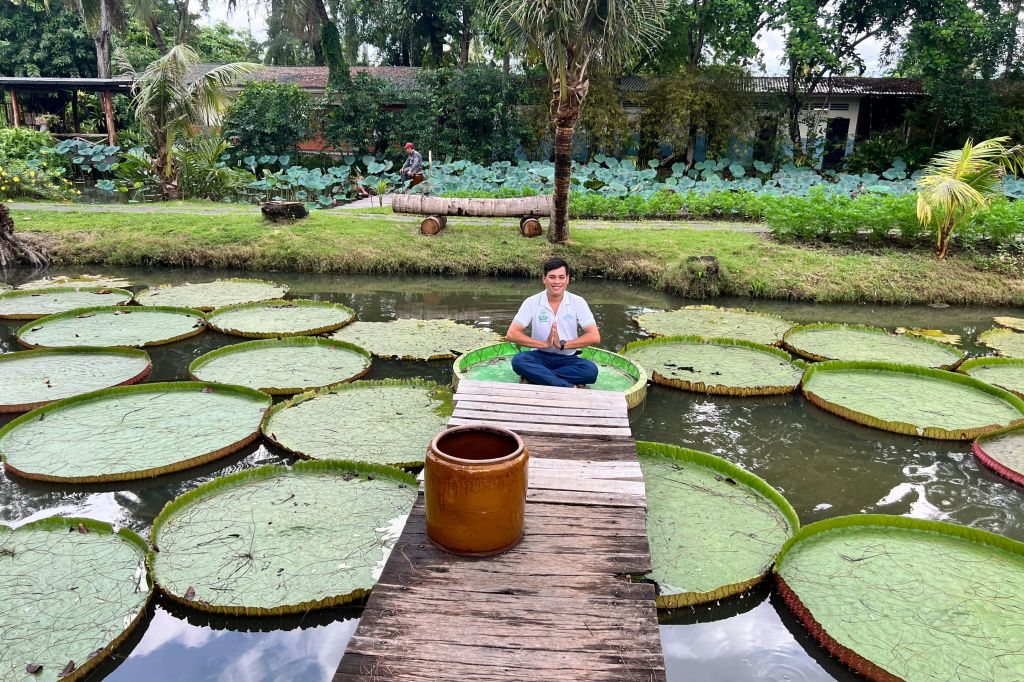 연못의 거대한 백합 패드에 다리를 꼬고 앉아 있는 사람으로 나무 산책로와 전경에 세라믹 냄비가 있습니다.