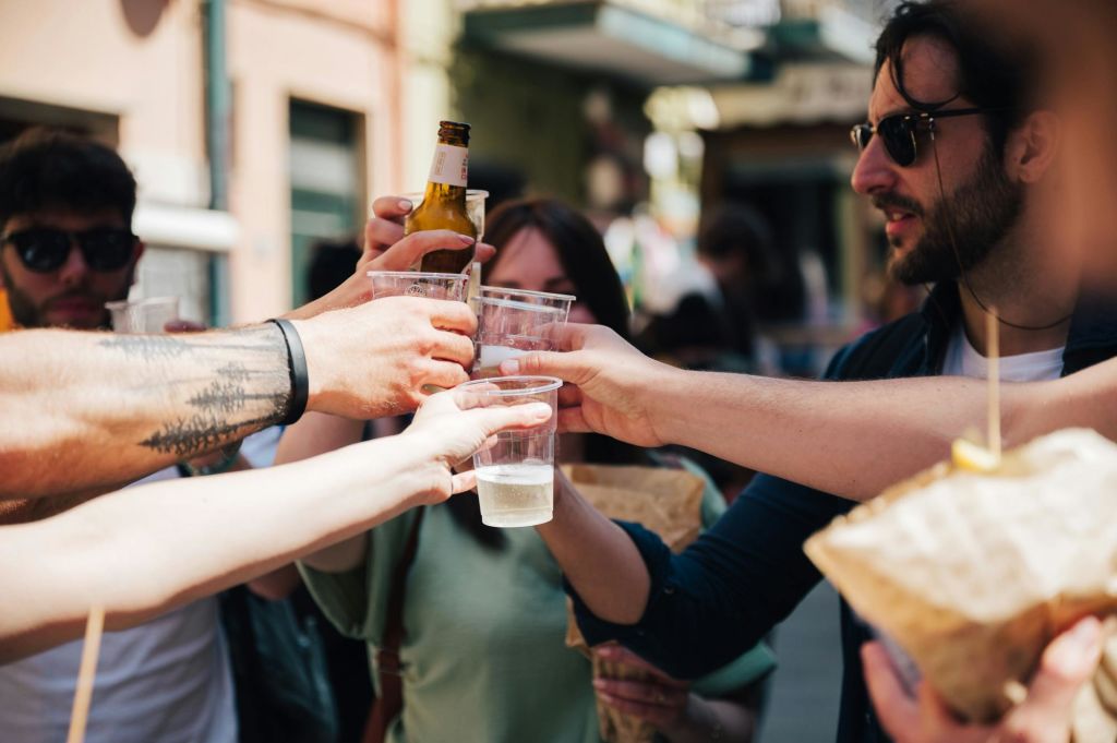 사람들이 야외에서 플라스틱 컵과 병을 핥고 있습니다. 한 사람이 음식 봉지를 들고 있습니다. 얼굴이 부분적으로 보입니다.