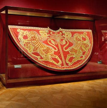 붉은 벽과 나무 바닥이 있는 박물관의 유리 케이스에 금사자 디자인의 붉은 의식용 방패가 전시되어 있습니다.