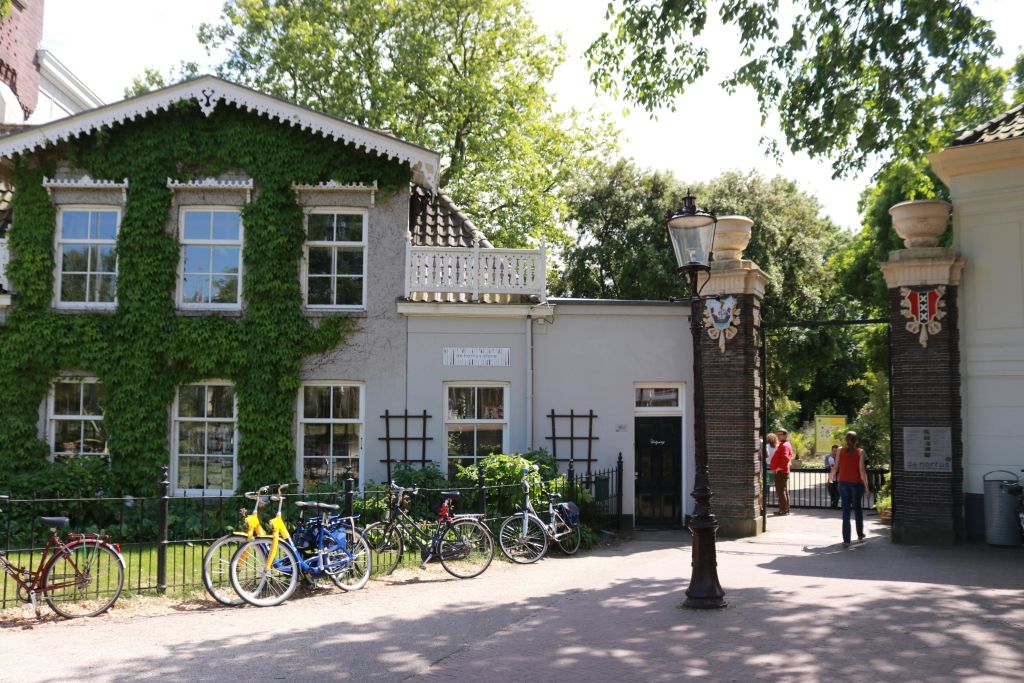 담쟁이 덩굴로 덮인 벽, 앞에 주차된 자전거, 햇살이 내리쬐는 하늘 아래 근처에 가로등이 있는 독특한 건물입니다.