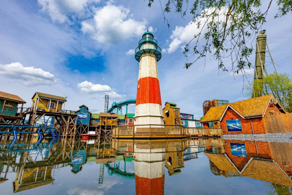 형형색색의 등대와 건물이 부분적으로 흐린 하늘 아래 고요한 물에 반사되어 푸르른 풍경이 펼쳐집니다.