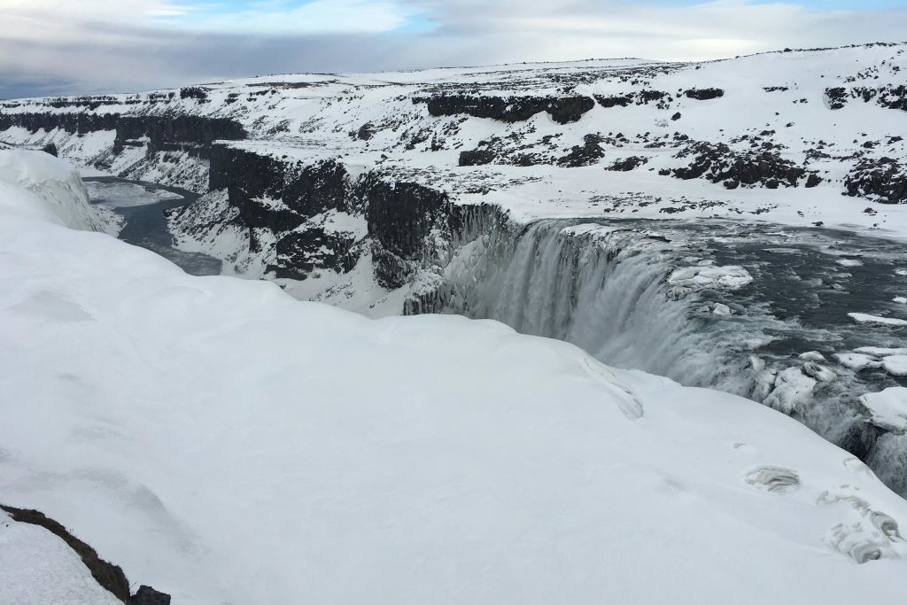 커다란 폭포가 절벽을 넘어 흐린 하늘 아래 눈 덮인 풍경으로 이어집니다.