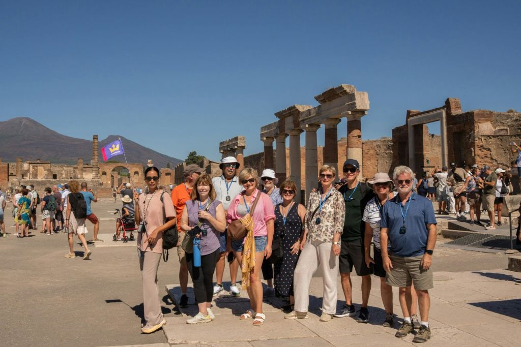 맑고 푸른 하늘 아래 기둥이 있는 고대 유적 앞에 관광객들이 모여 있습니다. 배경에는 더 많은 관광객이 보입니다.