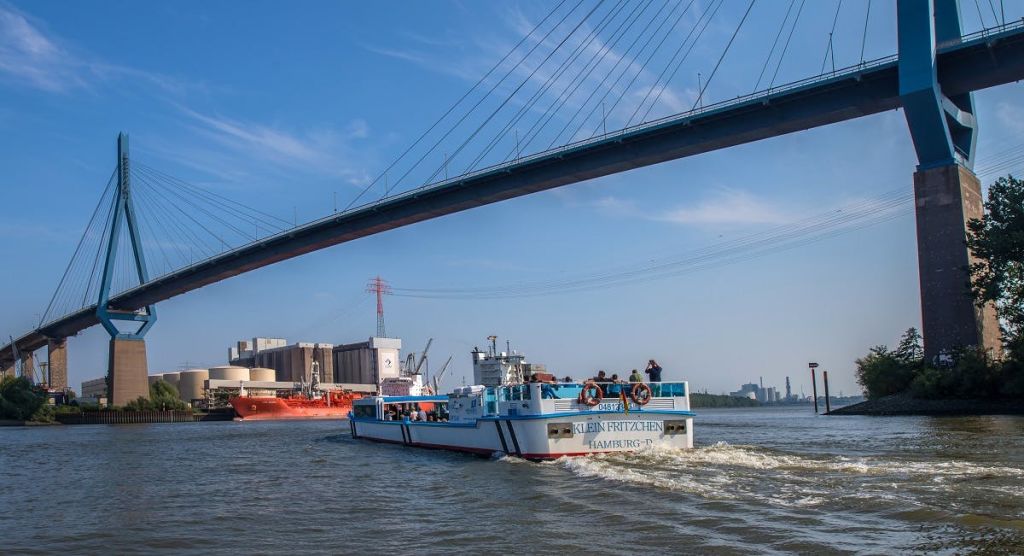 강에 "Kleiner Fritzchen Hamburg" 라고 표시된 선박으로 맑고 푸른 하늘 아래 산업 지역과 다리가 있습니다.