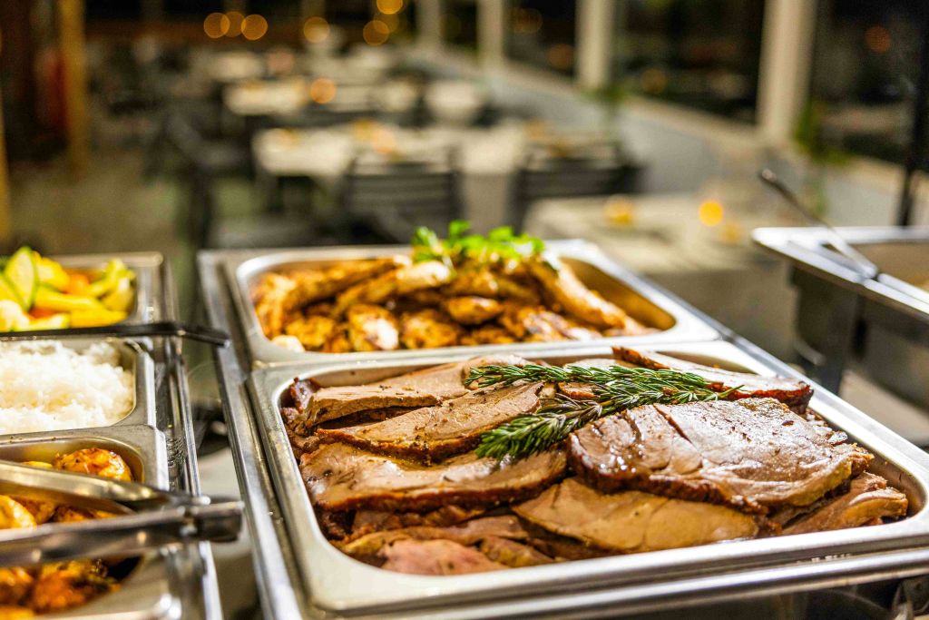 얇게 썬 고기 두 쟁반, 한 쟁반은 허브로 장식되어 있으며, 뷔페를 배경으로 식사 공간이 흐릿합니다.