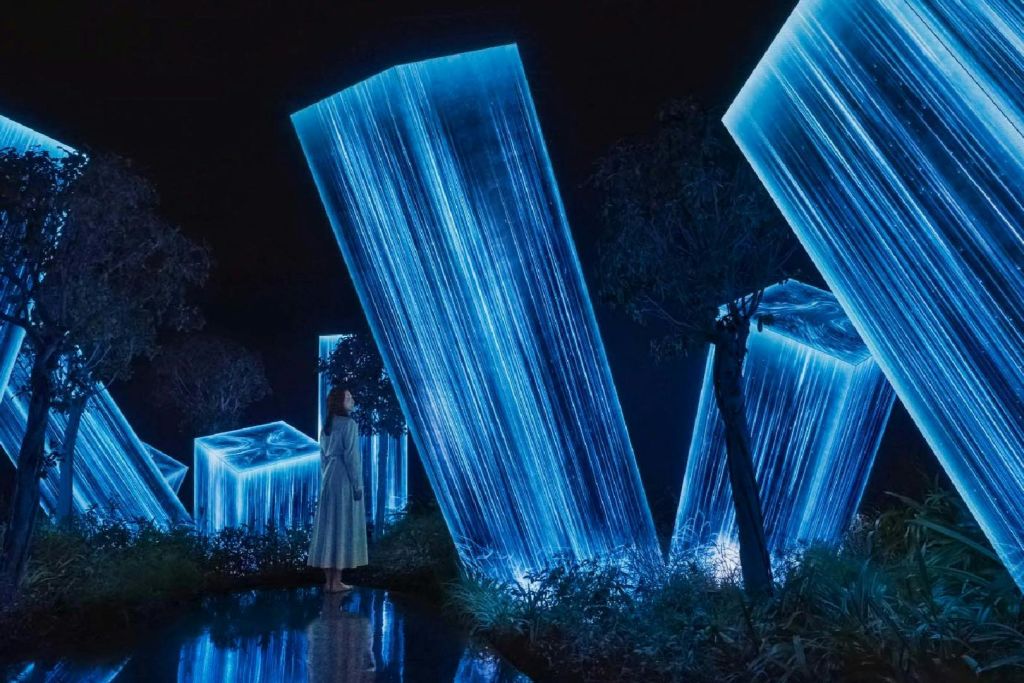 한 여성이 빛나는 푸른색 크리스탈 구조물과 나무로 둘러싸인 어두운 환경에 서 있습니다.