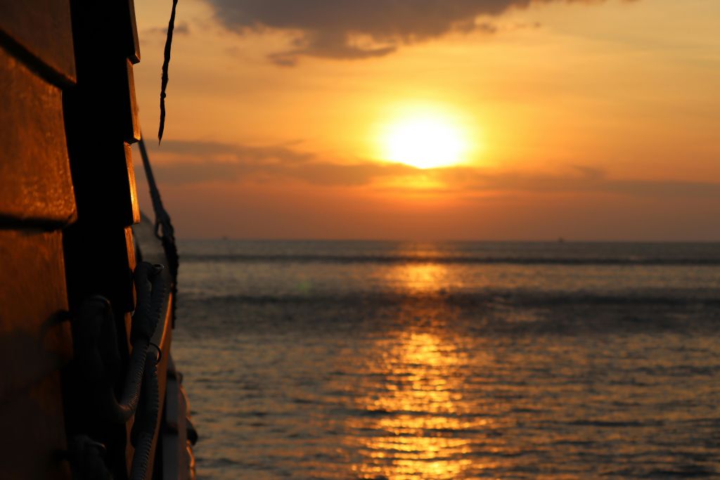 주황색 구름이 있는 바다 위로 해가 지고, 왼쪽에 보트가 부분적으로 보입니다.