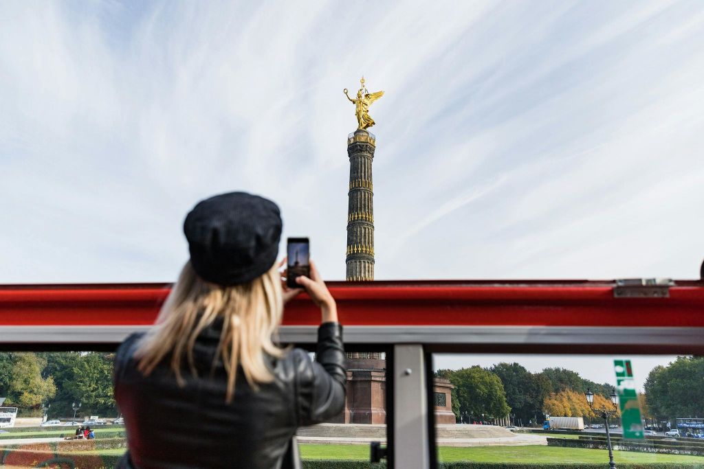 검은 모자와 재킷을 입은 사람이 파란 하늘을 배경으로 금상이 그려진 높은 기둥의 사진을 찍고 있습니다.