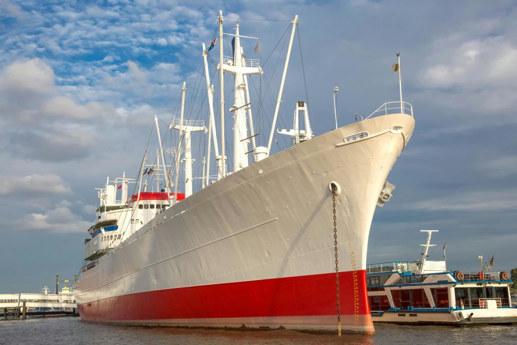 푸른 하늘과 구름을 배경으로 물가에 정박한 흰색과 빨간색의 대형 선박.
