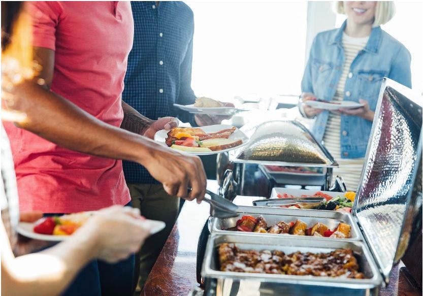 사람들은 뷔페 테이블에서 음식을 제공하고 접시를 들고 서빙 기구를 사용합니다.