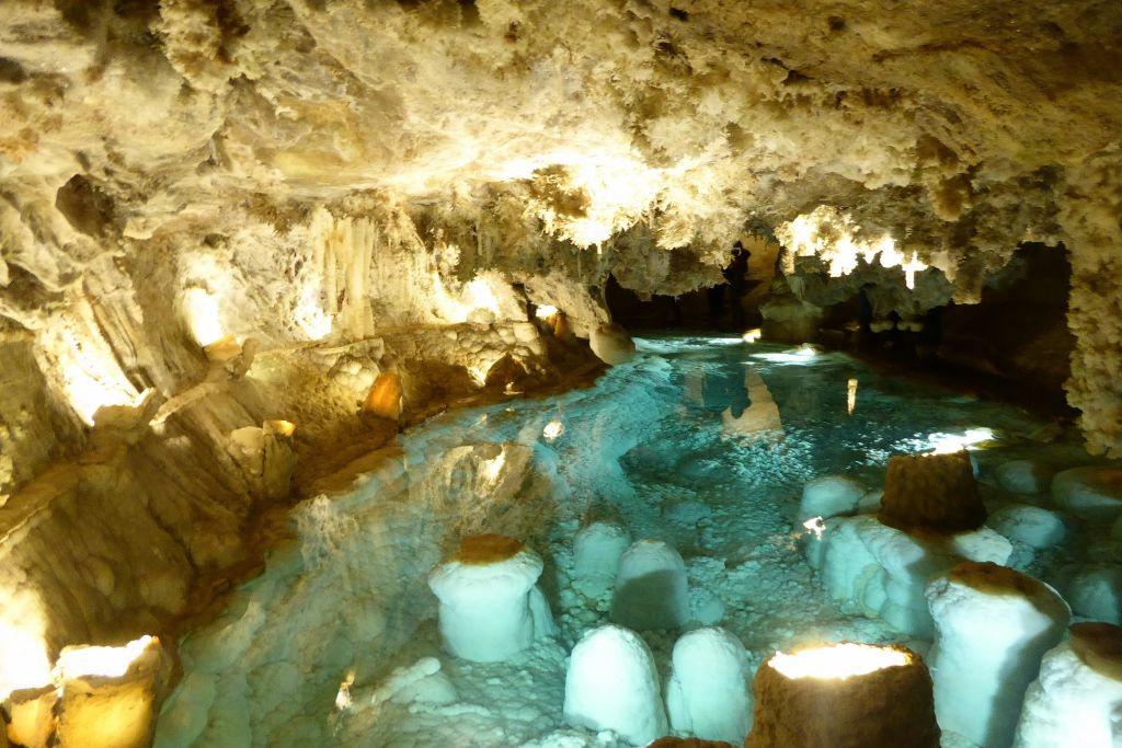 조명이 있는 종유석과 종유석이 있는 동굴과 수면에 반사되는 투명한 파란색 지하 수영장이 있습니다.