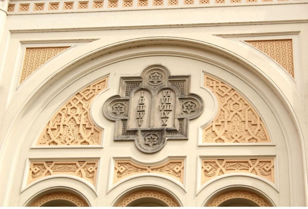 베이지색과 흰색 아치 안에 로마 숫자와 장식 별이 세팅된 두 개의 태블릿이 특징인 화려한 건축 디테일.