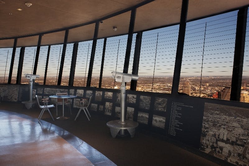 대형 창문, 망원경, 의자가 있는 작은 테이블이 있는 전망대. 창문을 통해 보이는 도시 풍경.