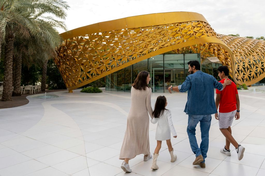 한 가족이 금색 외관을 장식한 현대적인 건물을 향해 걸어가고 있습니다.