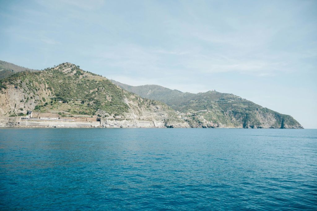맑은 하늘 아래 산악 지형의 해안선을 배경으로 잔잔한 푸른 바다.