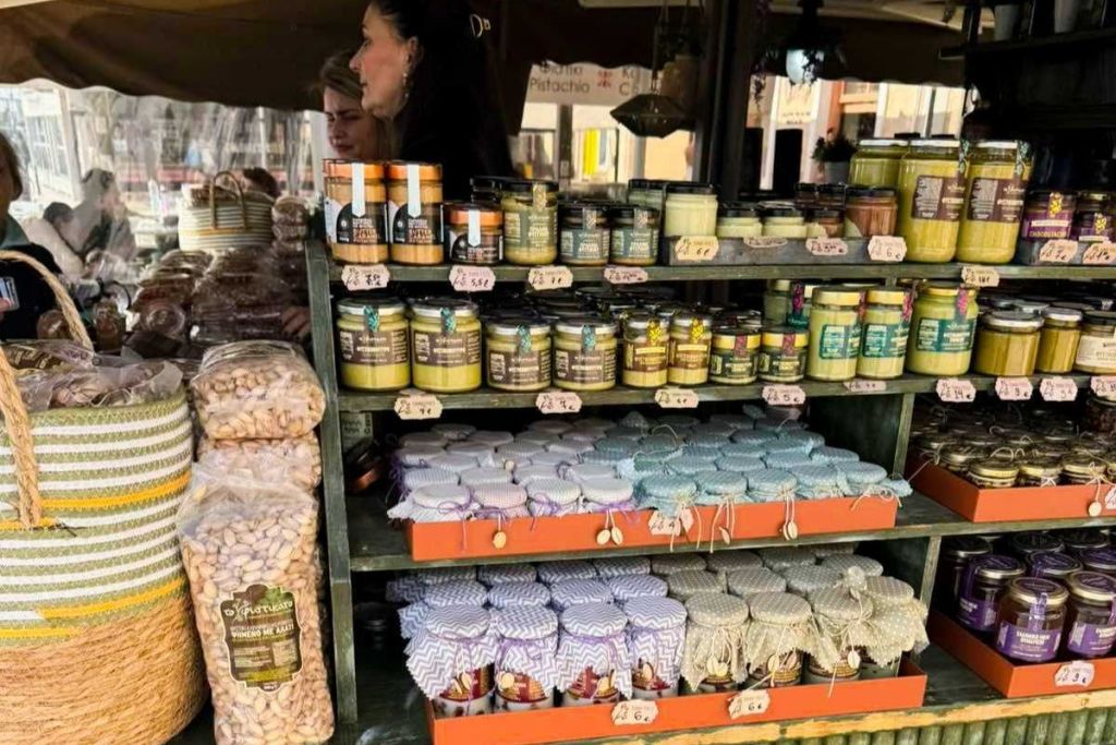 꿀병, 젓갈, 포장 견과류가 진열된 선반이 있는 시장 가판대입니다. 배경에는 두 사람이 보입니다.