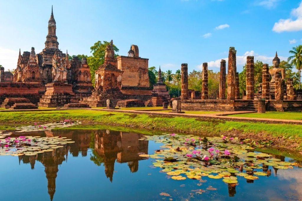 녹음으로 둘러싸인 벽돌 구조물과 석조 기둥이 있는 고대 사원 유적은 수련이 있는 연못에 반사됩니다.