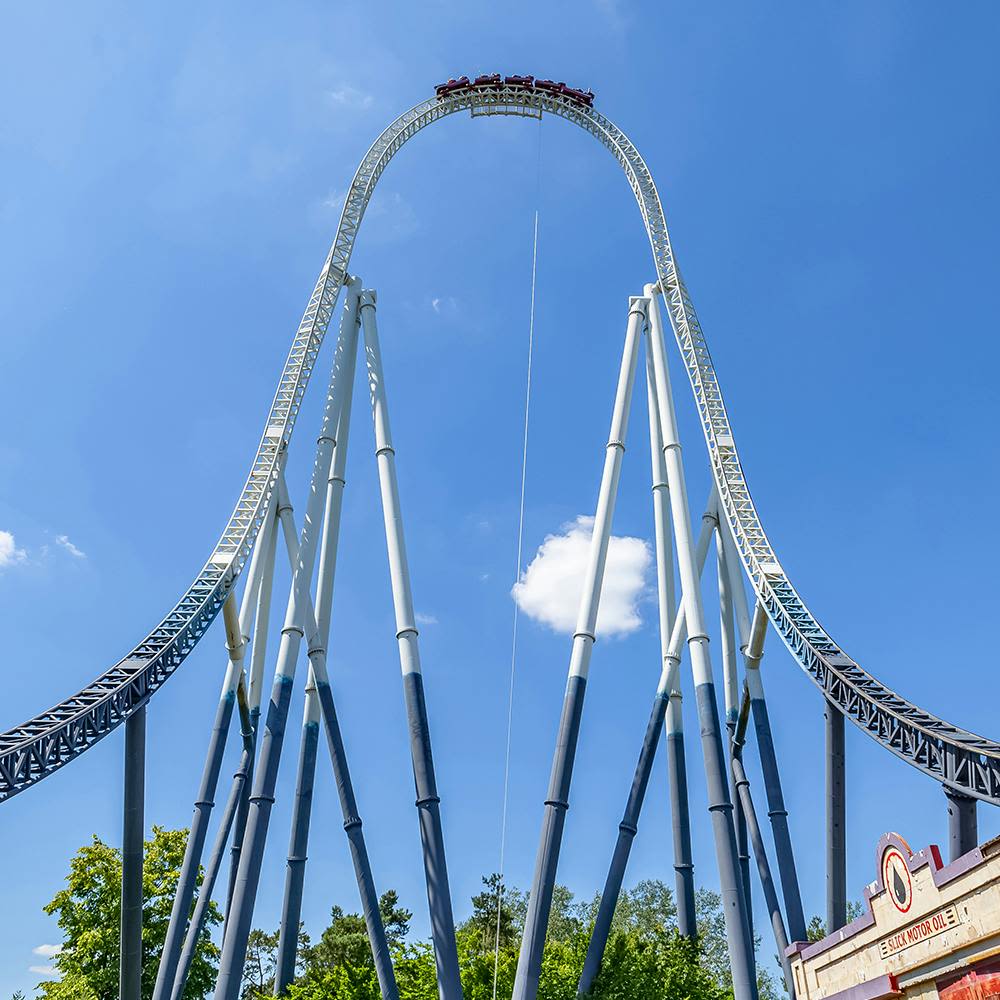 푸른 하늘을 배경으로 수직으로 높이 솟은 롤러코스터에 나무가 몇 그루 있고 바닥에 부분적인 건물이 있습니다.