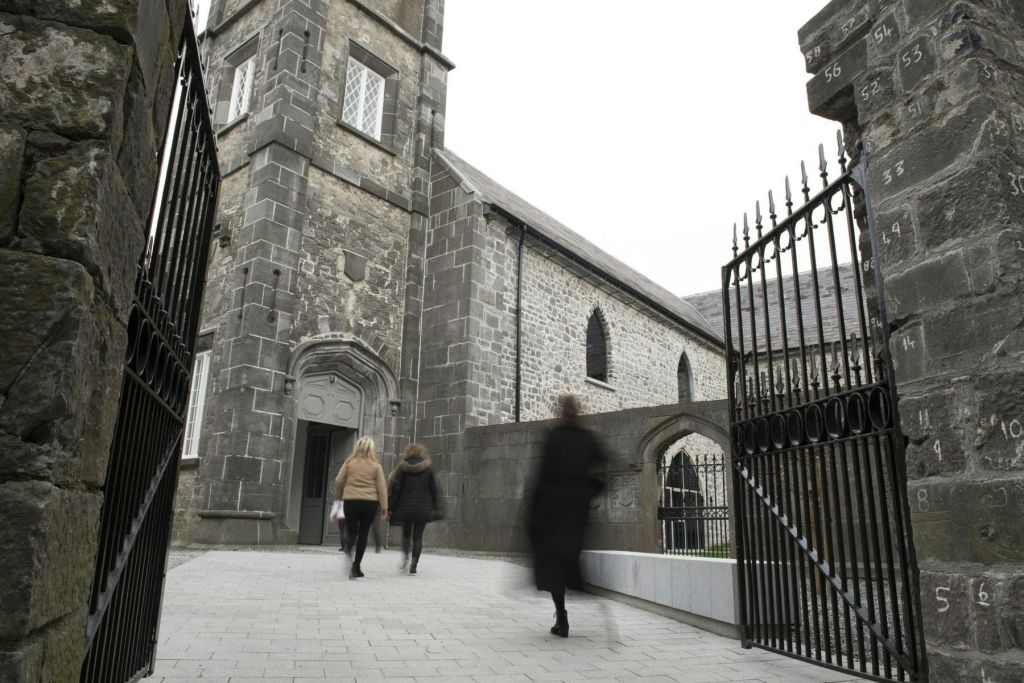 개방된 연철문을 통해 오래된 석조 교회 건물을 향해 걸어가는 세 사람.
