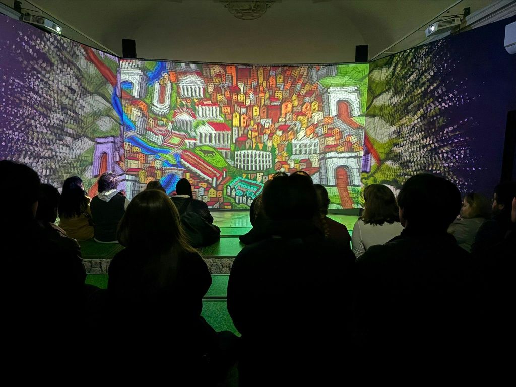 사람들이 실내에 앉아 주변의 대형 스크린에서 활기차고 다채로운 도시 풍경을 감상하고 있습니다.