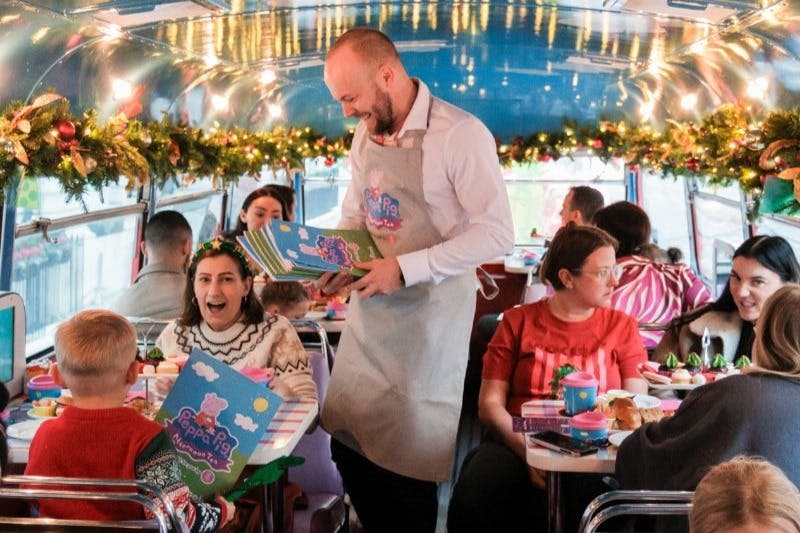 화환으로 장식된 버스의 축제 인테리어로 테이블에 사람들이 앉고 서버가 테마 메뉴를 나눠줍니다.