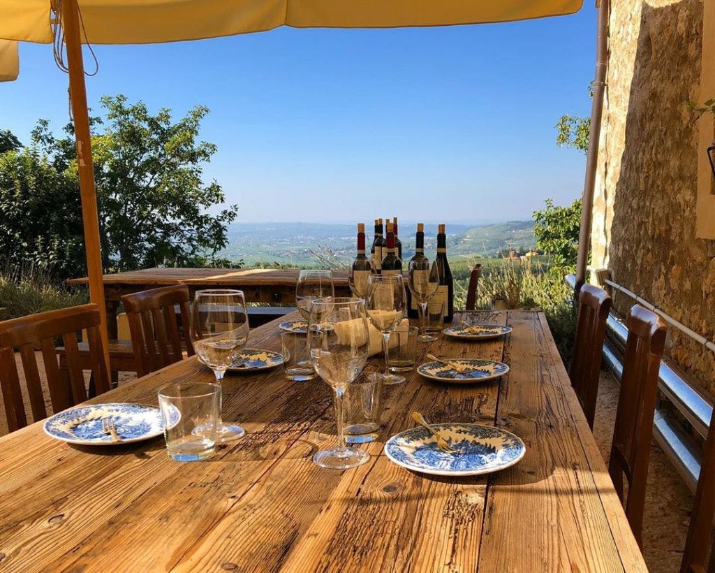 빈 와인잔, 부스러기가 담긴 접시, 여러 병의 와인병이 놓인 야외 소박한 테이블. 아름다운 시골 풍경을 배경으로