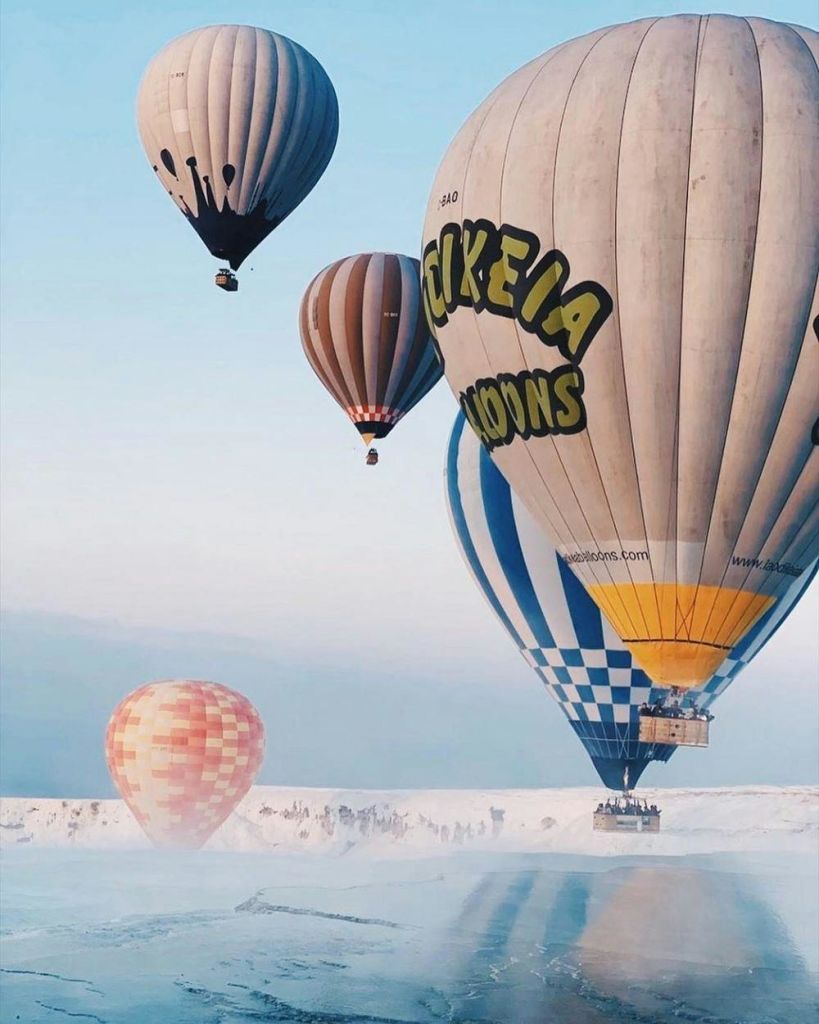 눈 덮인 풍경 위로 푸른 하늘에 떠 있는 다양한 색상과 패턴의 열기구.